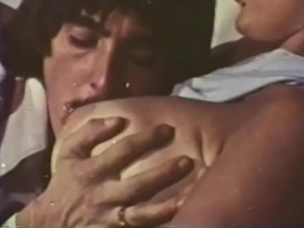 A mustachioed dude with long sideburns caresses an experienced blonde with huge buckets in a 70s video